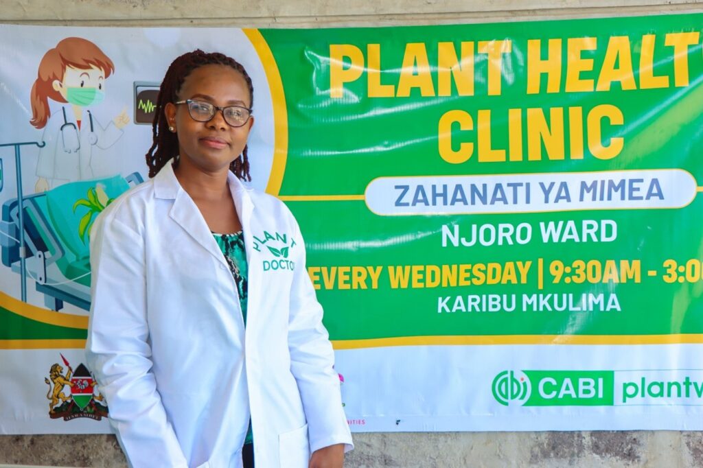 Plant doctor Florence Malemba standing next to her plant clinic banner.
