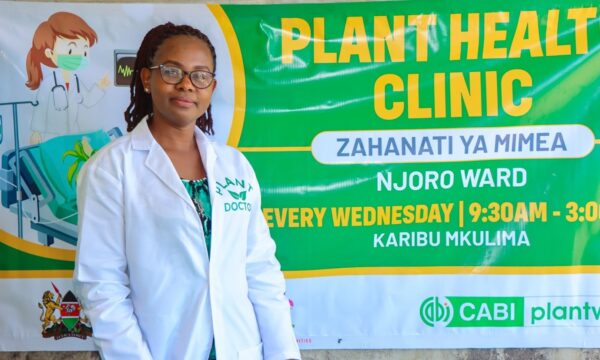 Plant doctor Florence Malemba standing next to her plant clinic banner.