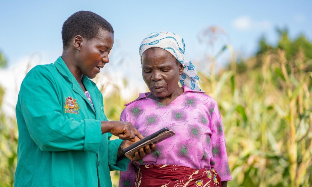 An extension officer showing a farmer some information on a digital device